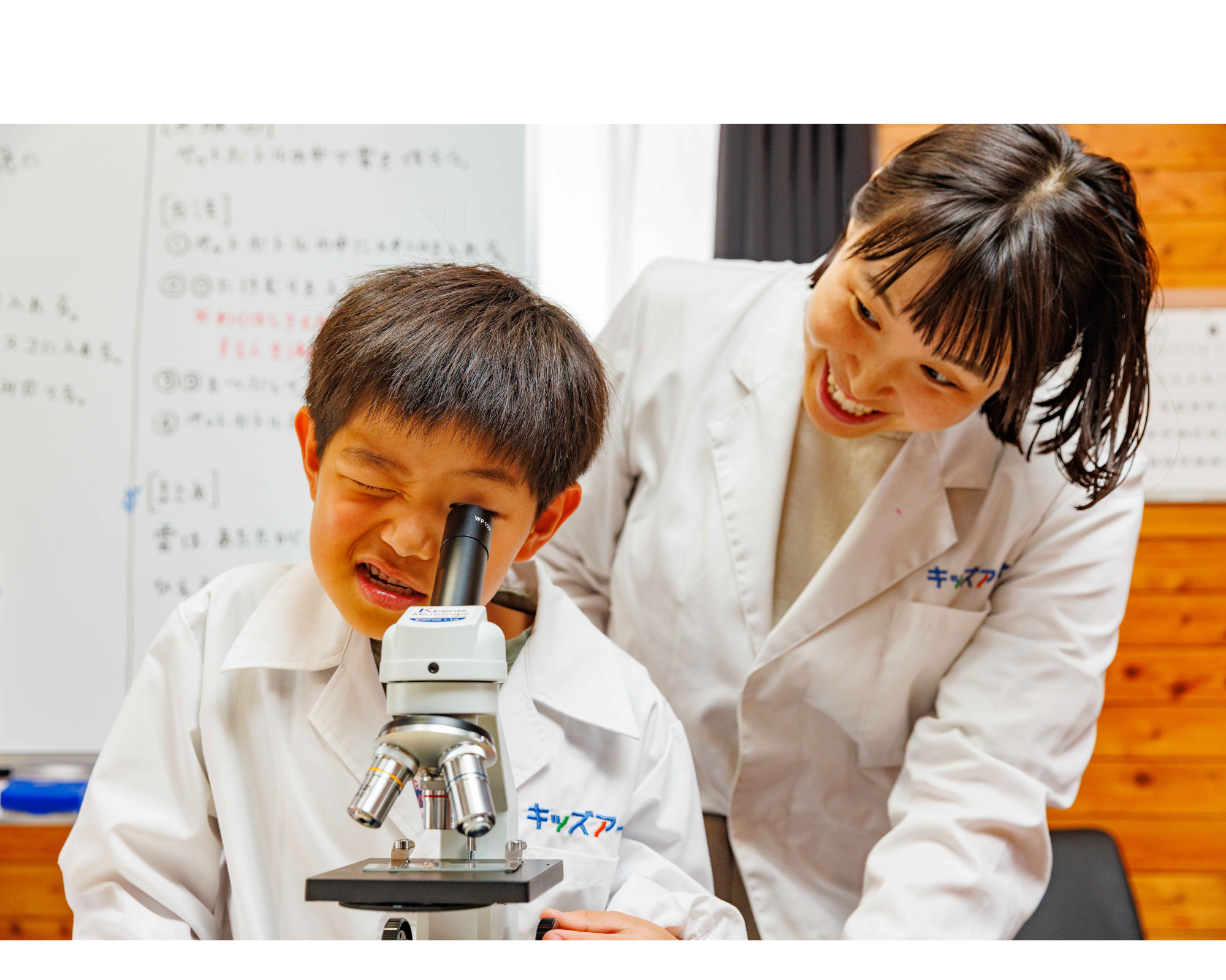 顕微鏡をのぞく子どもとそれを見守る先生